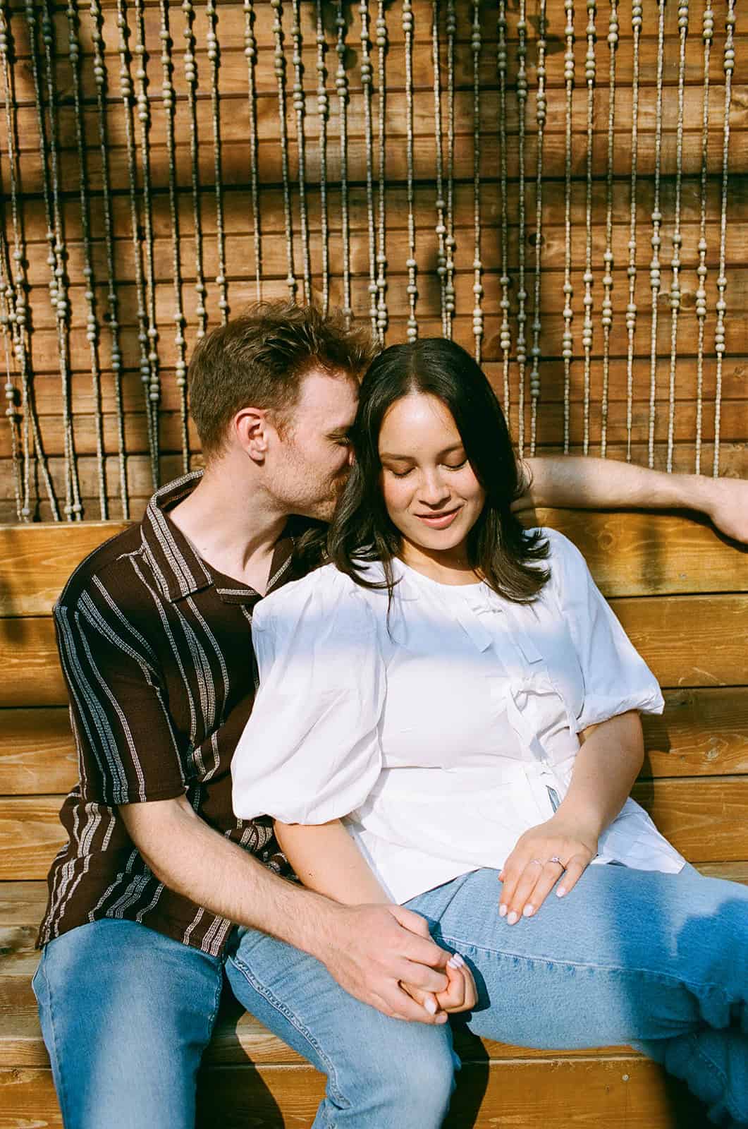 couple snuggles on the patio of Mrs Robinson in little italy during engagement session